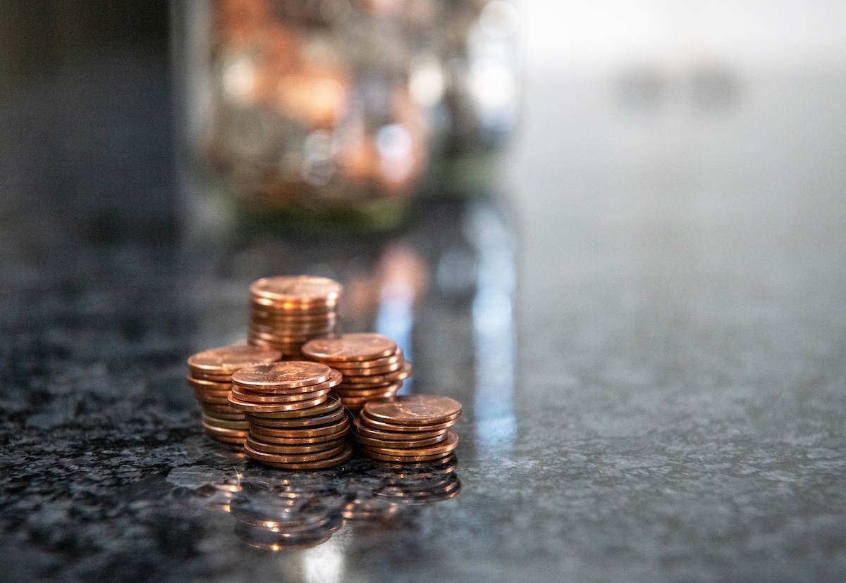 A stack of pennies on a kitchen counter with a jar of coins in the background.