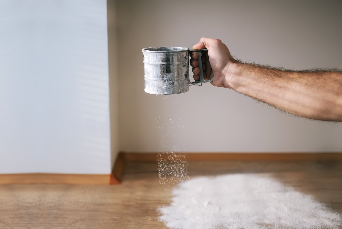 Hand sifting flour onto wood floor.