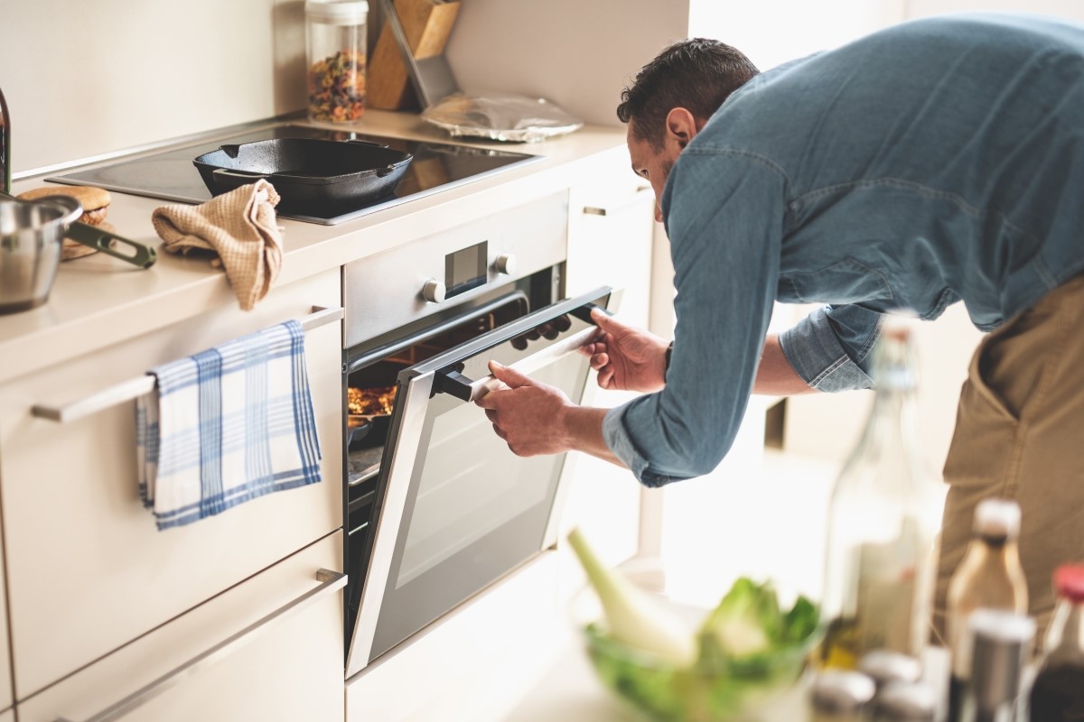 Portrait of gentleman in denim shirt closing door of oven.