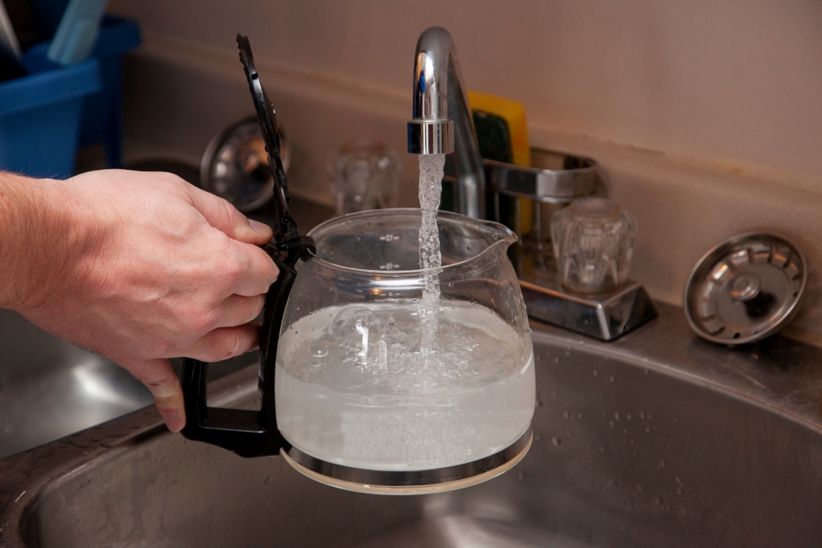 A person filling up their coffee pot with tap water.