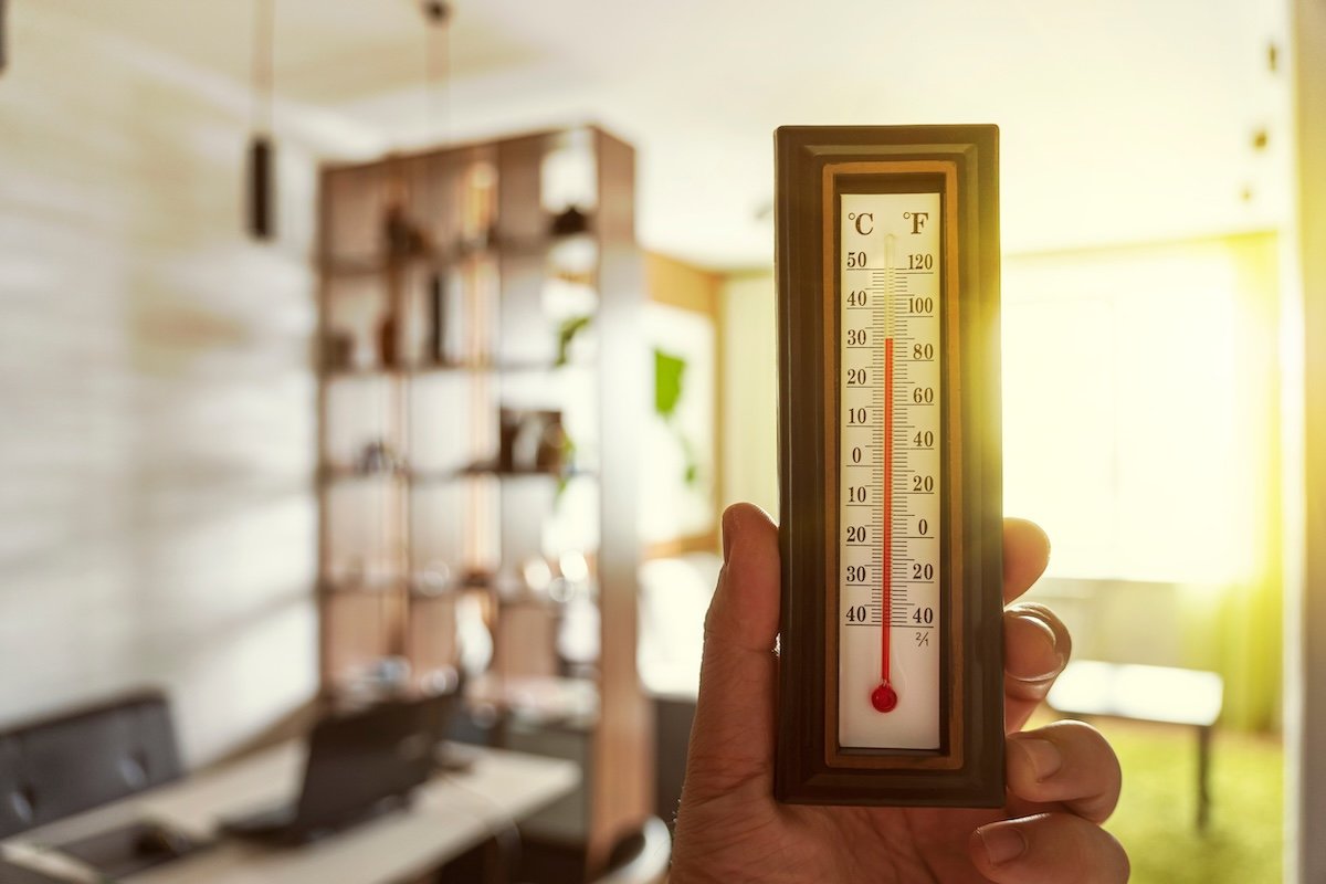 Person holding thermometer inside house to show heat during summer.