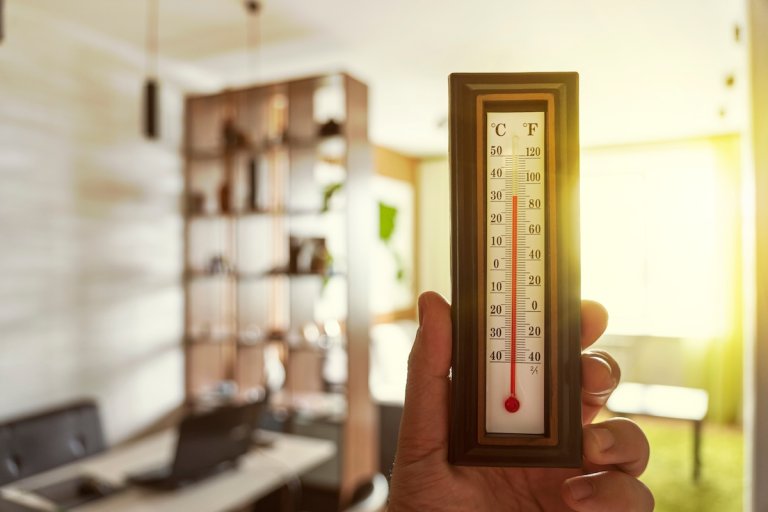 Person holding thermometer inside house to show heat during summer.