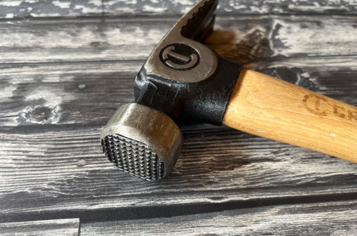 Close view of the head of a faming hammer on a wood table.
