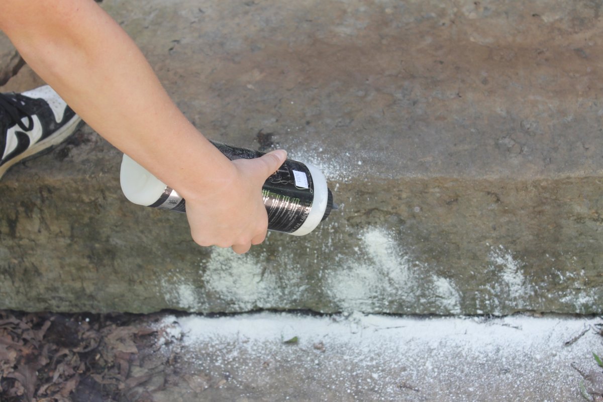 A person sprinkling Dr. Killigan's ant killer around a porch perimeter during testing