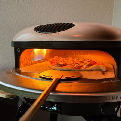 A person pulling a pizza out of the Gozney Arc XL during testing