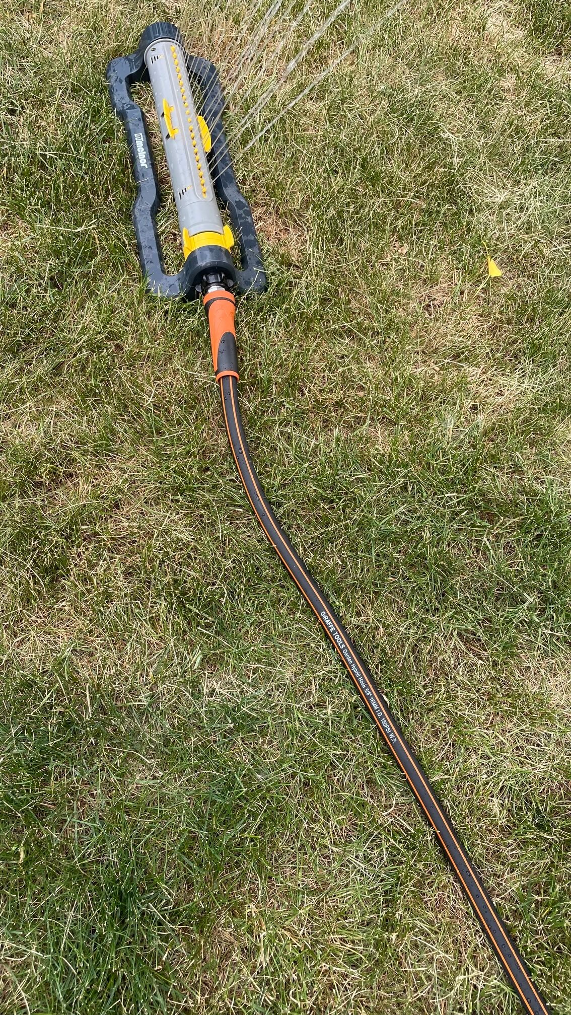 The Giraffe Tools Hybrid Garden Hose With Swivel Handle connected to a sprinkler