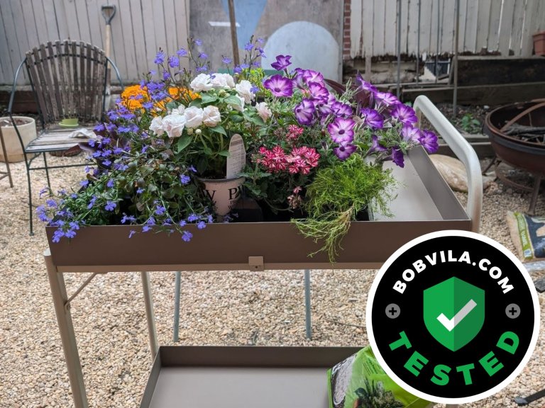 The Vego Garden Potting Cart holding potted blooming plants in a gravel patio