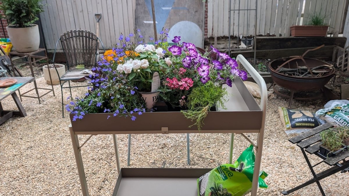 The Vego Garden potting cart full of blooming plants in pots on a pea gravel patio