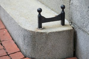 Iron boot scraper embeeded in front cement step near brick pathway.