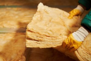 Person holding a layer of yellow batt insulation, about to lay it on attic floor.