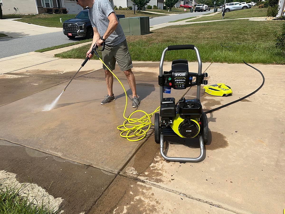 A person using one of the best Ryobi pressure washers to clean a cement driveway
