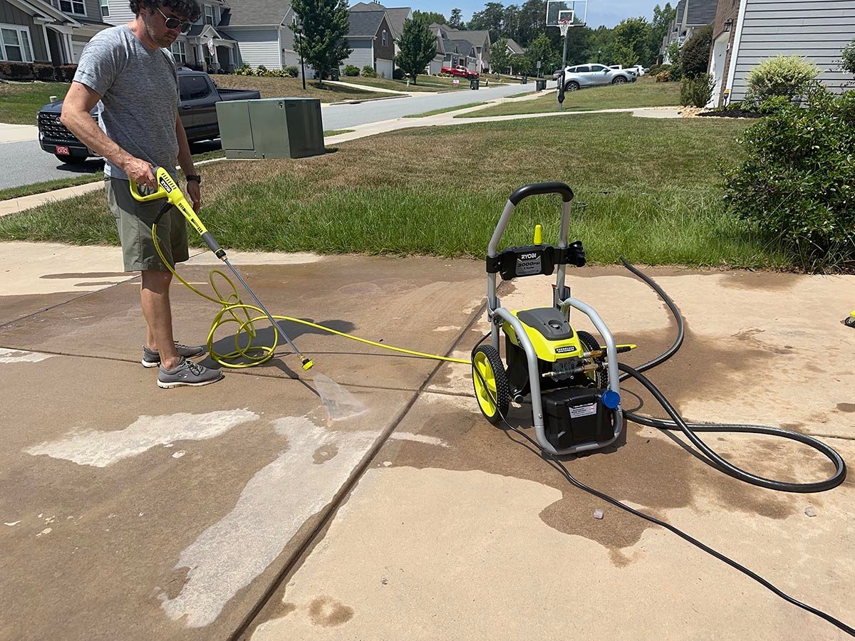A person using one of the best Ryobi pressure washers to clean a cement driveway