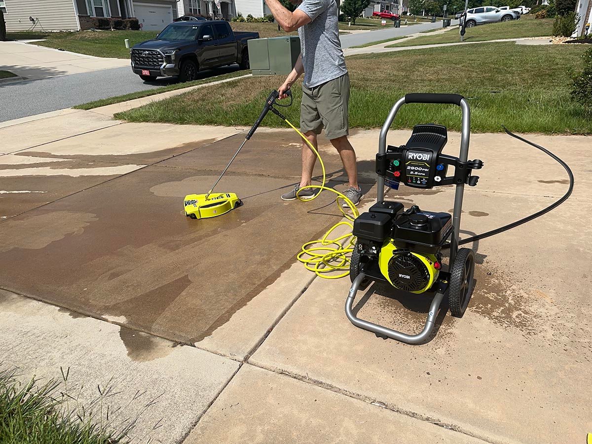 A person using one of the best Ryobi pressure washers to clean a cement driveway