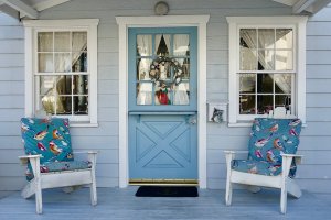 Blue Dutch door on a blue beach house, with two Adirondack chairs on either side of the door.