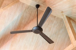 Electric vintage ceiling fan hanging from a wood paneled, vaulted ceiling.