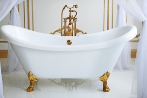 A white claw foot tub with gold feet and a gold faucet in an opulent, antique-looking bathroom.