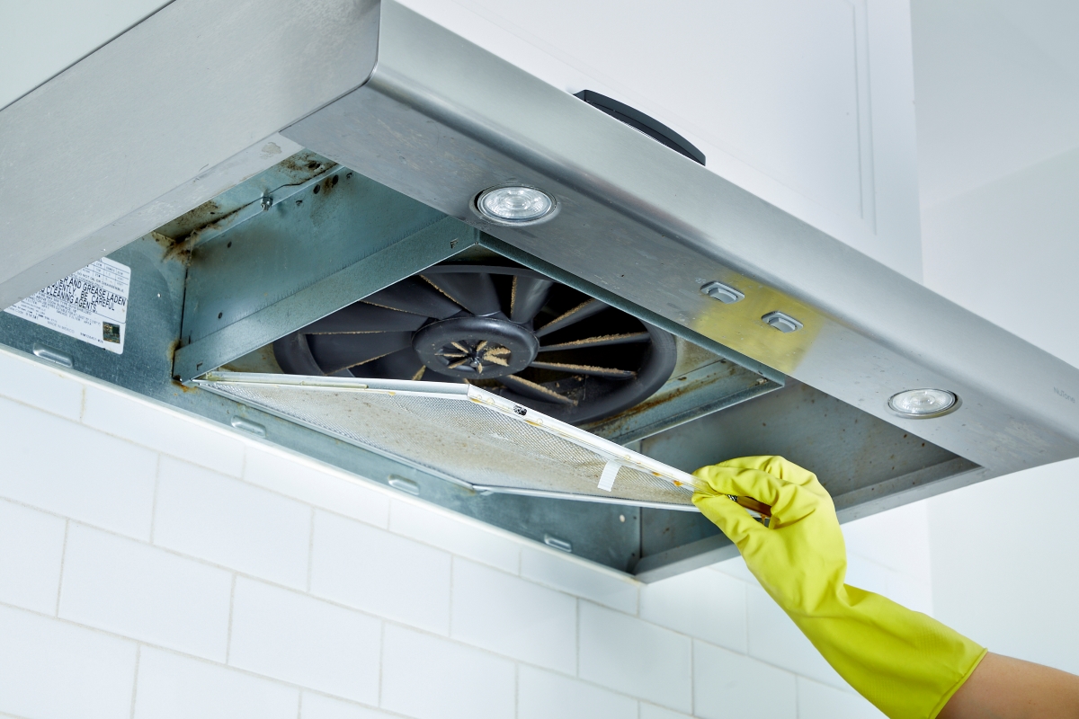 A gloved hand is cleaning a range hood.