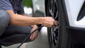 Man crouching to fill air in the tires of his car.
