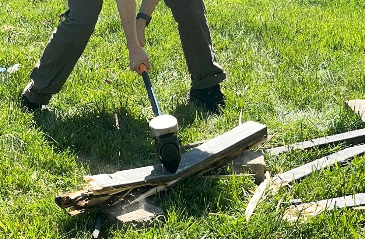 Man uses sledgehammer to break wood boards in a backyard.