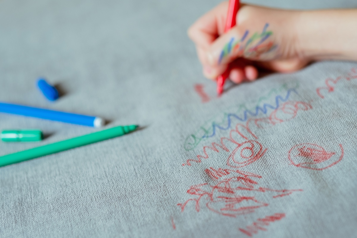 A child uses permanent markers to drawn on a fabric sofa. 