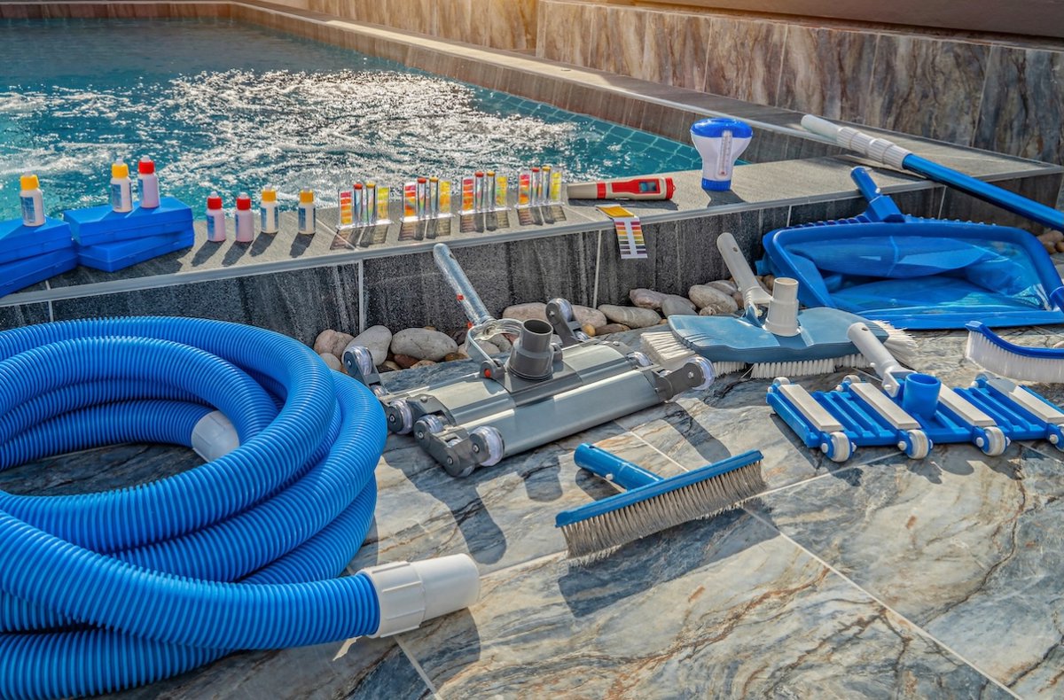 Hoses, vacuums, pool test kits, and other pool cleaning accessories neatly lined up on the edge of a luxury swimming pool.