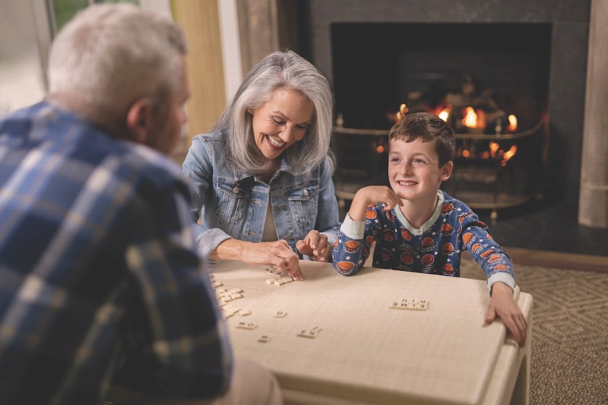 Grandparents and grandchild playing a game with a propane fireplace in the background keeping them warm.