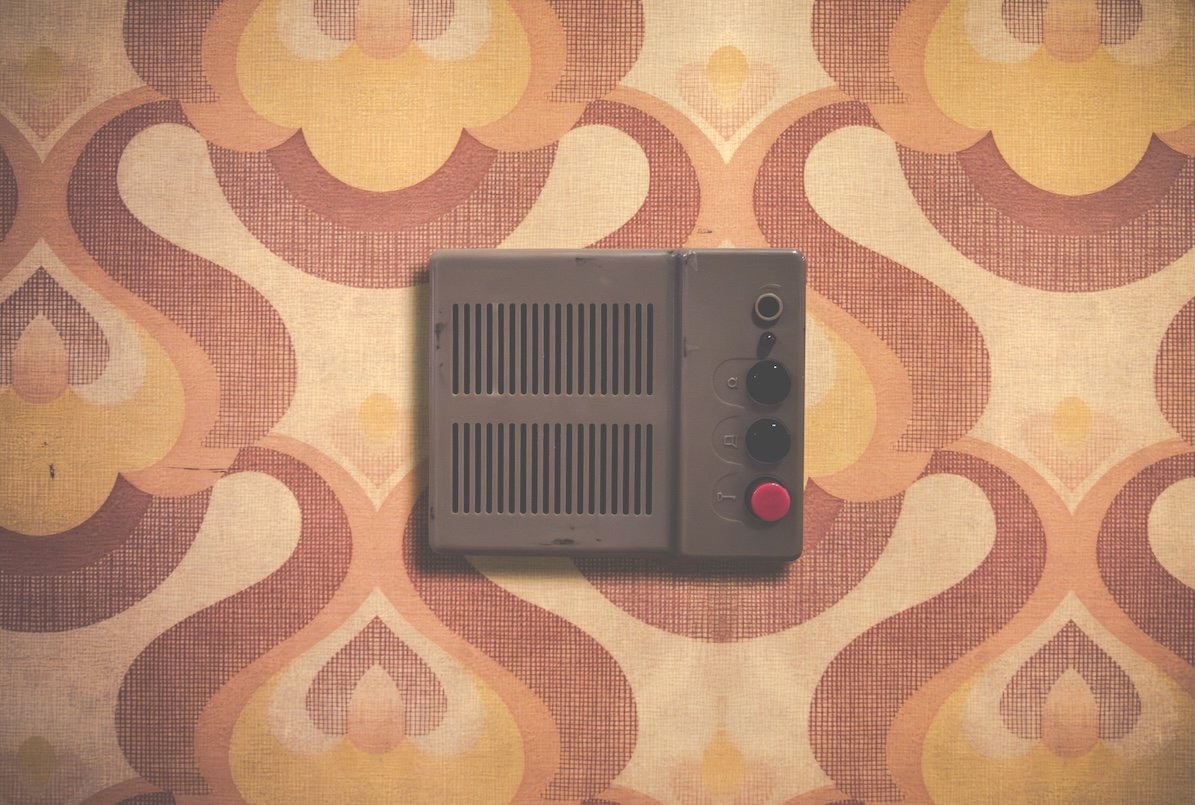 Vintage metal intercom on retro 1970s patterned wallpaper.