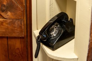 Old black rotary phone, in on hold position, sitting, in hallway phone nook