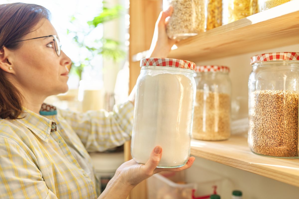 Woman holding a glass container filled with flour in her pantry
