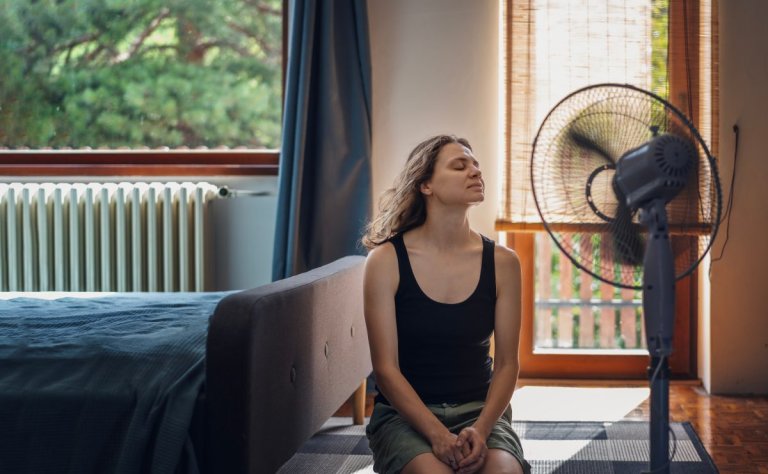 Young woman suffering from heat sitting at home on the floor in front of a fan.