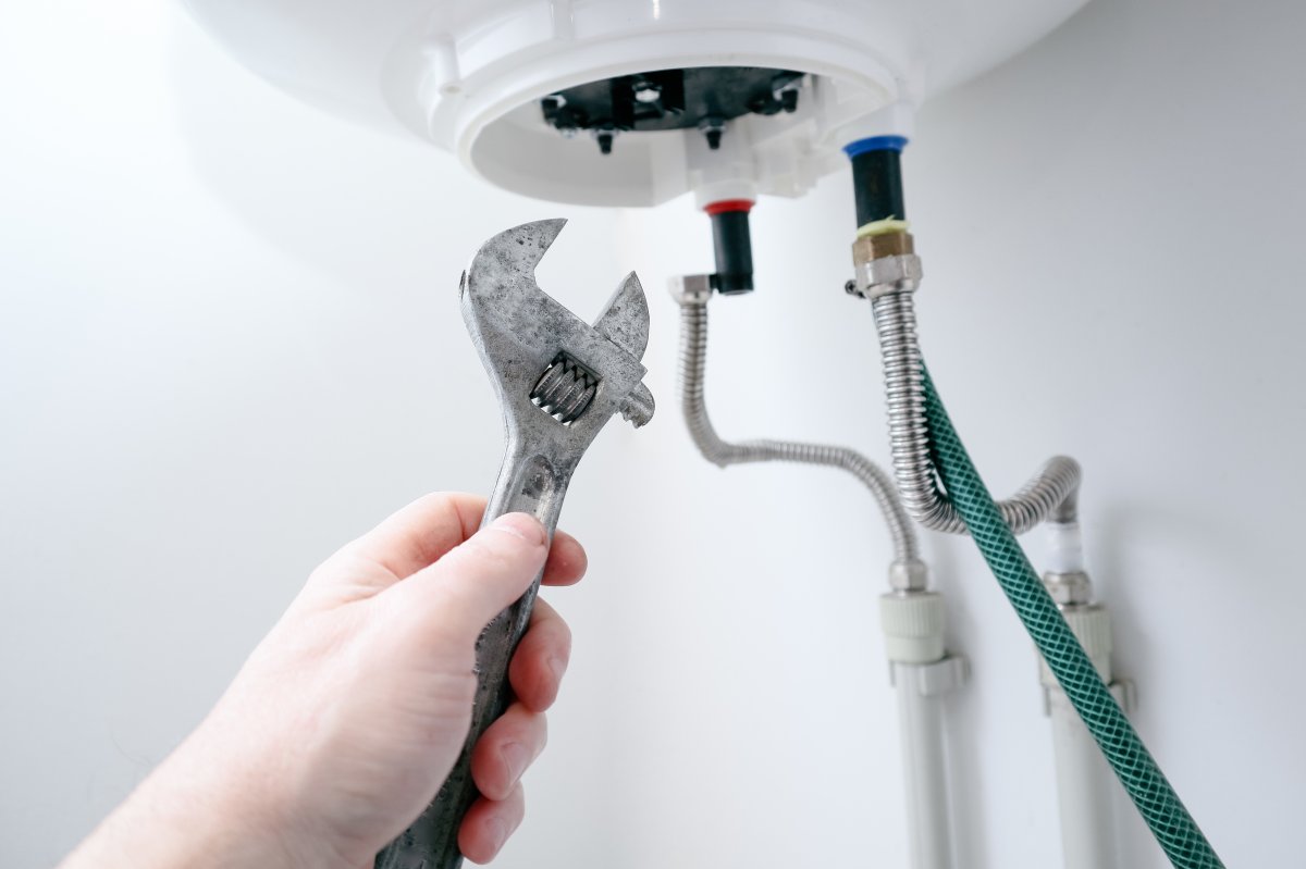 Close up of a hand holding a wrench in front of a water heater.