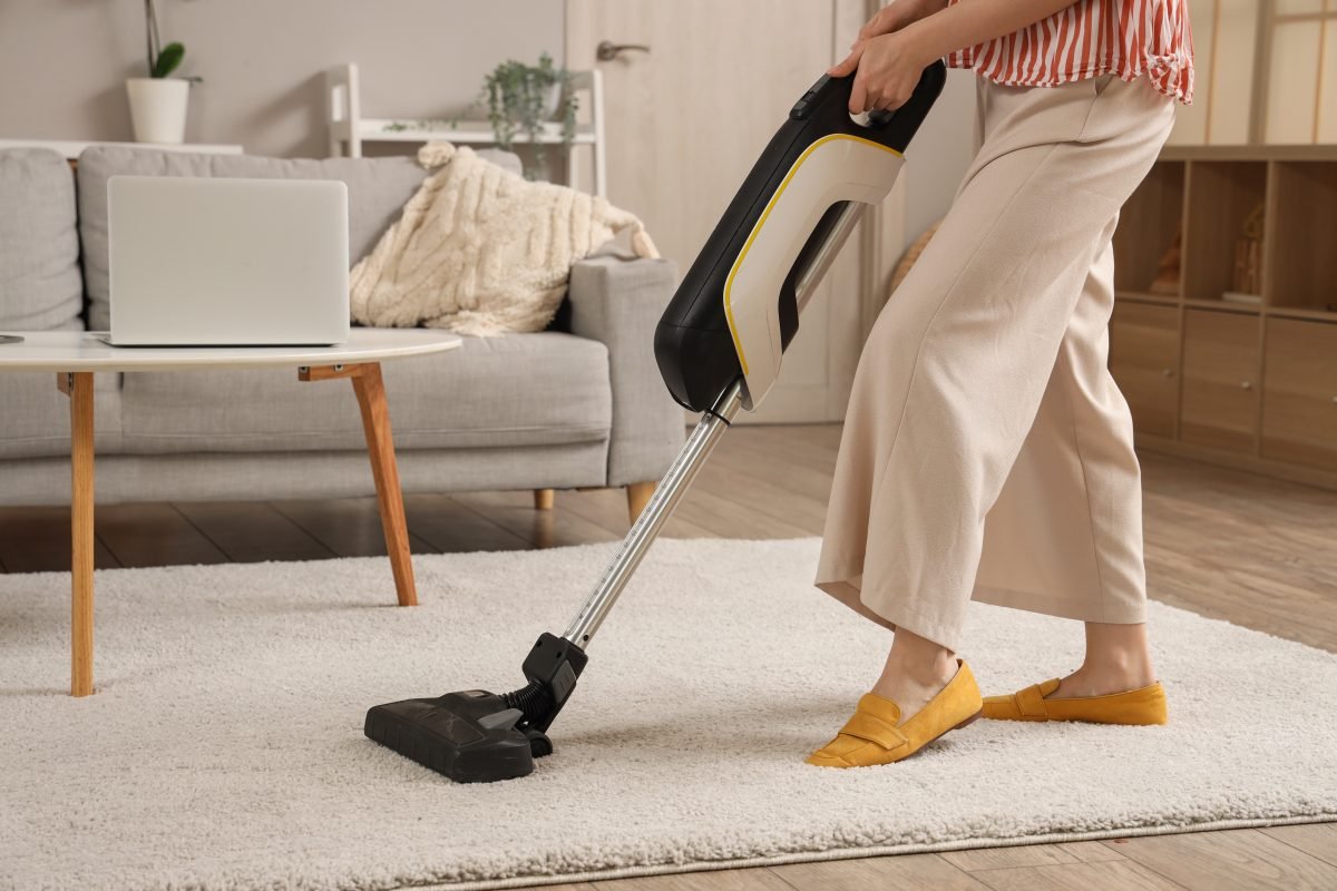 Woman cleaning carpet with cordless stick vacuum cleaner in living room.