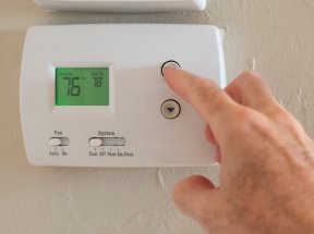 Person adjusting the temperature on a thermostat that reads 76 degrees.
