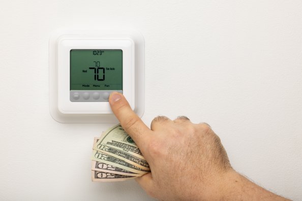 Man adjusting the temperature on a thermostat holding $20s and $50s in his fist