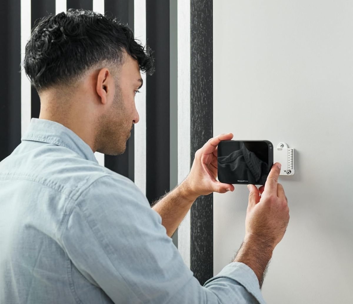 Man sets up a Honeywell thermostat on the wall of his home