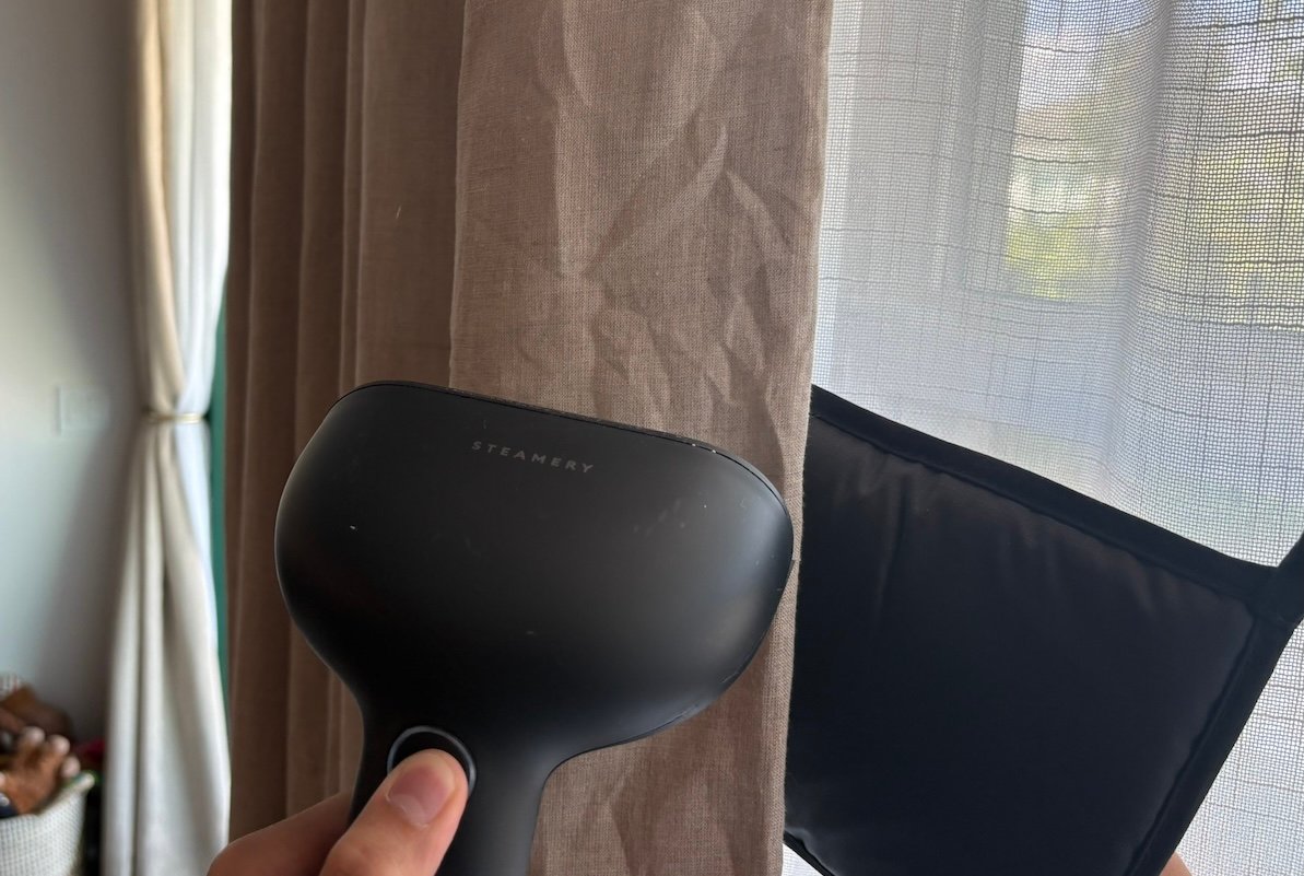Person uses handheld steamer to steam wrinkles out of brown bedroom curtains.