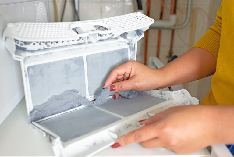 A woman with painted nails cleans lint from the lint trap of a dryer.