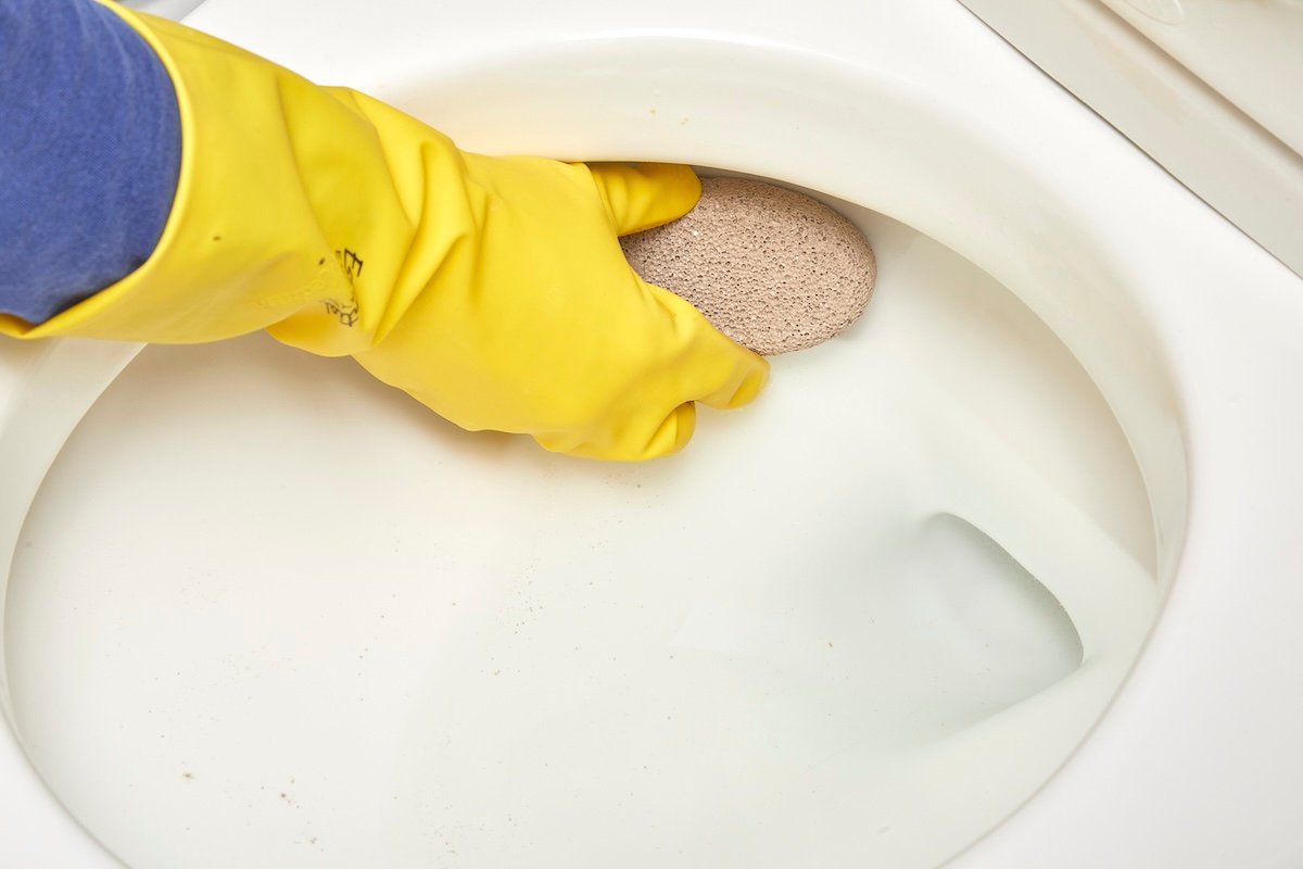 Using a pumice stone to clean the inside of a toilet bowl.
