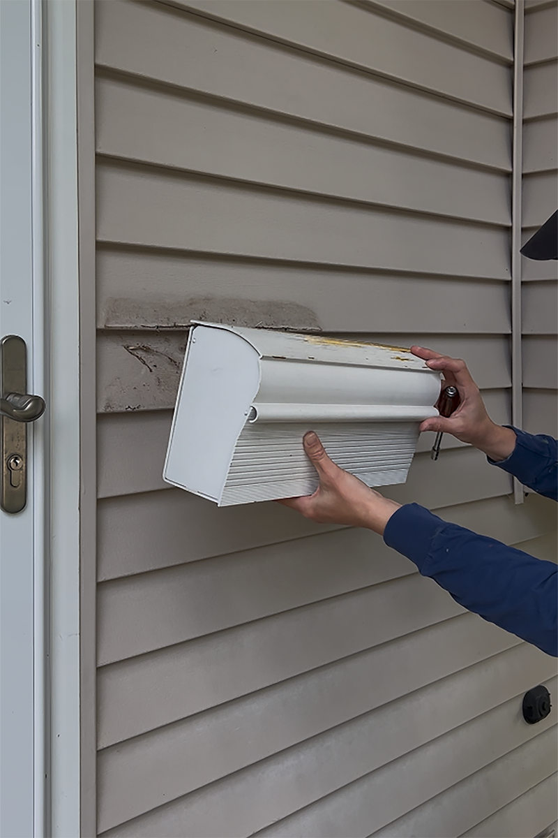 A DIYer removing a tired mailbox from the front of a house.