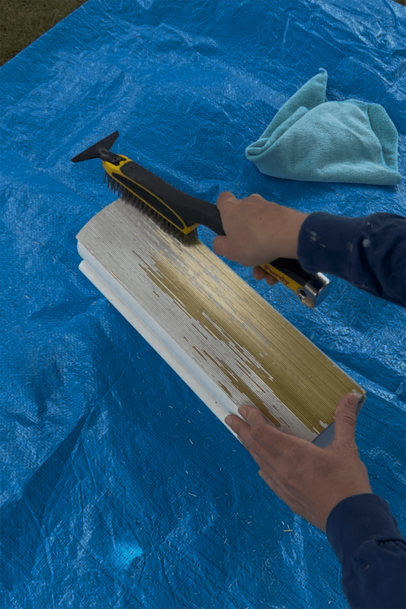 A DIYer using a wire brush to scrape off peeling paint on a mailbox.