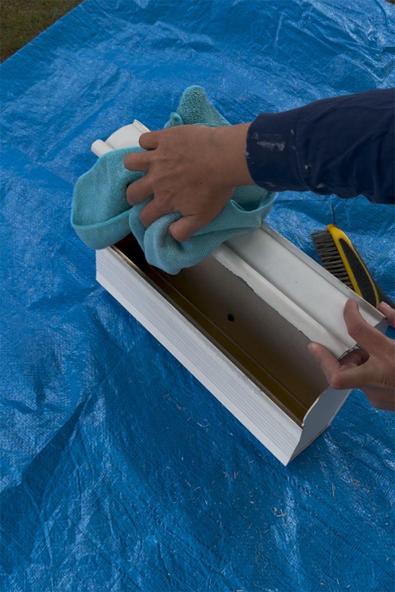 A DIYer using a microfiber cloth to clean a mailbox before painting.