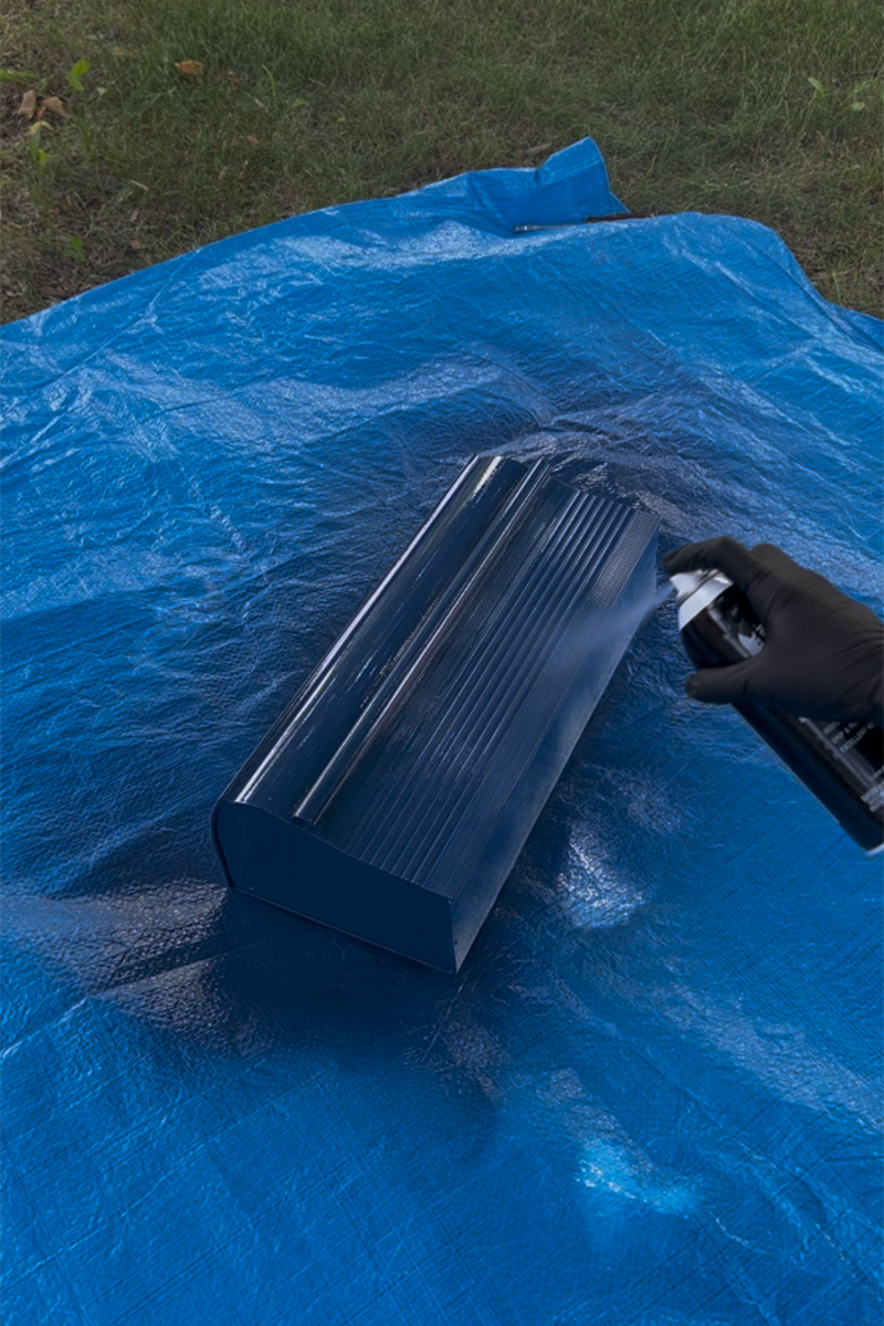 A DIYer using blue spray paint to paint a mailbox.