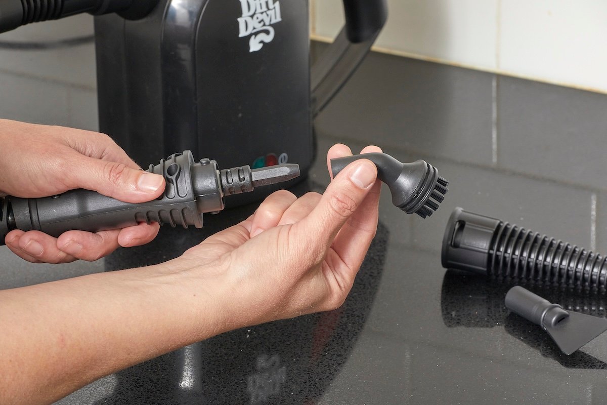 Woman attaches small nylon brush head on steam cleaner attachment handle.