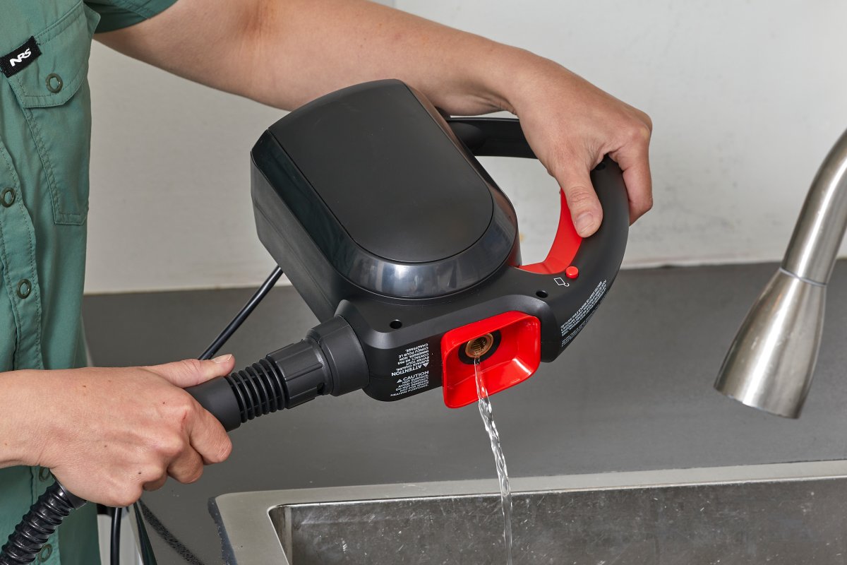 Woman dumps water out of a black steam cleaner into a kitchen sink.