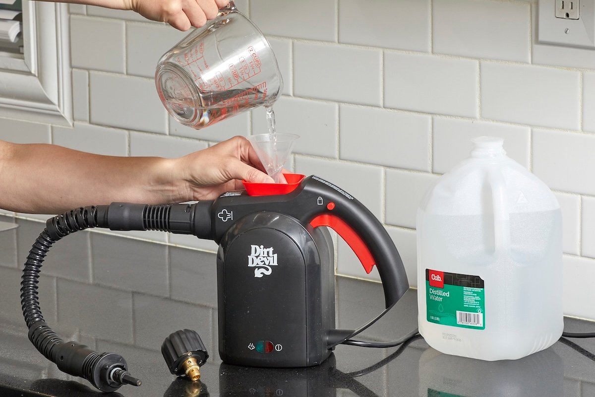 Woman uses a measuring cup to pour distilled water through a funnel into a handheld steam cleaner.