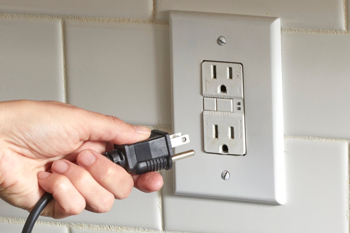 Close up view of a woman plugging an appliance into an outlet.