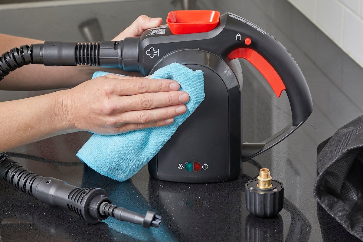 Woman uses a blue microfiber cloth to wipe a handheld steamer.