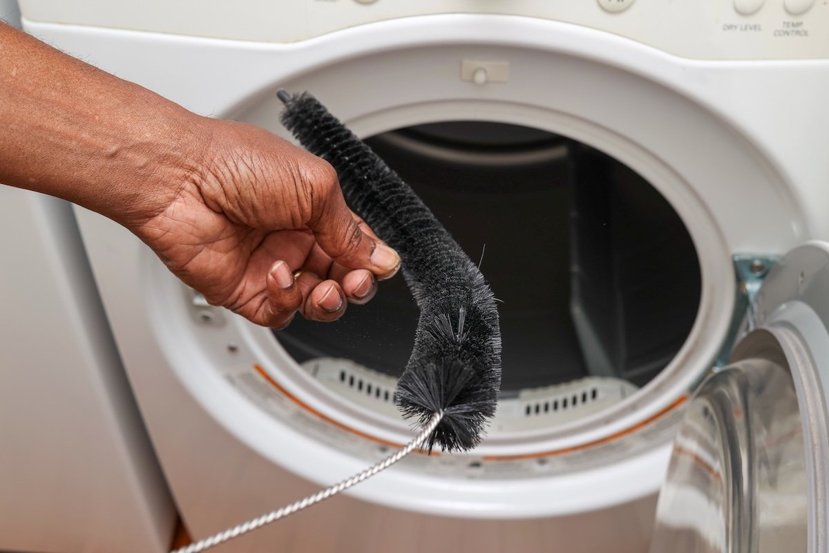 A man uses a lint trap brushed to loosen the debris in a dryer. 