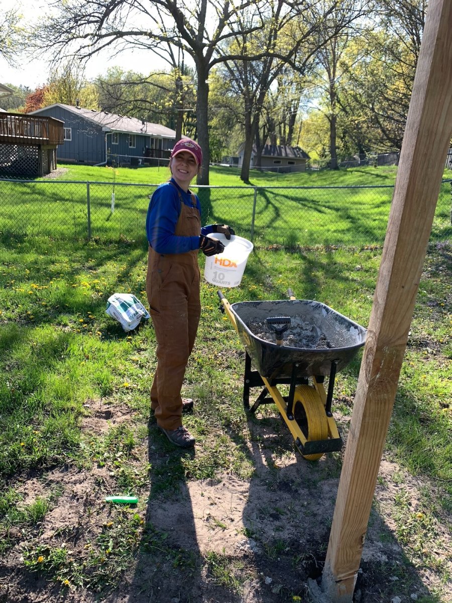 Executive Editor Jenny Stanley mixing concrete in a wheelbarrow for setting fence posts.
