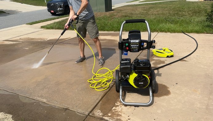 Man uses a Ryobi pressure washer to wash a cement driveway.